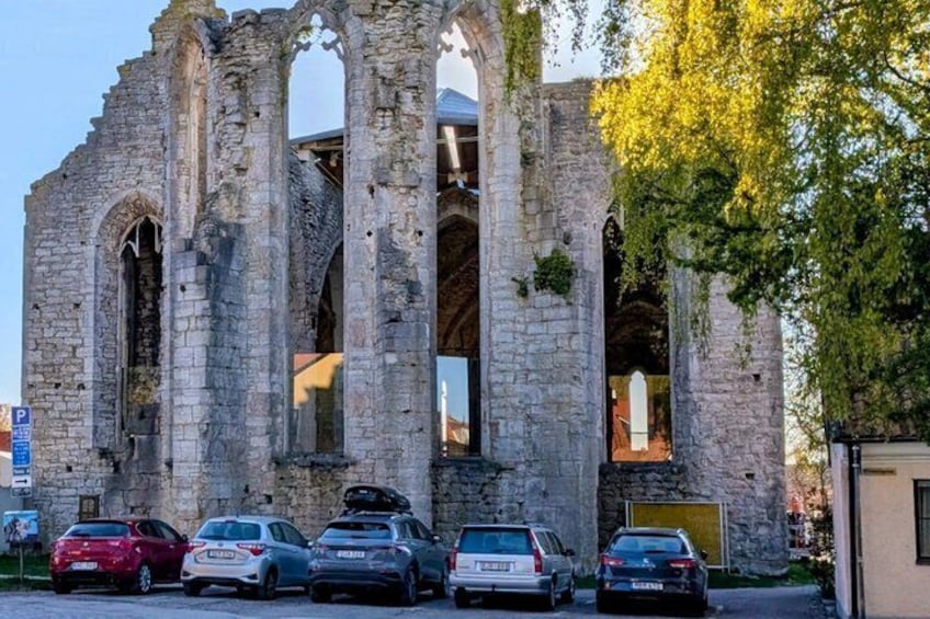 A historic stone structure with arches, parked cars, and a tree in the foreground. 3