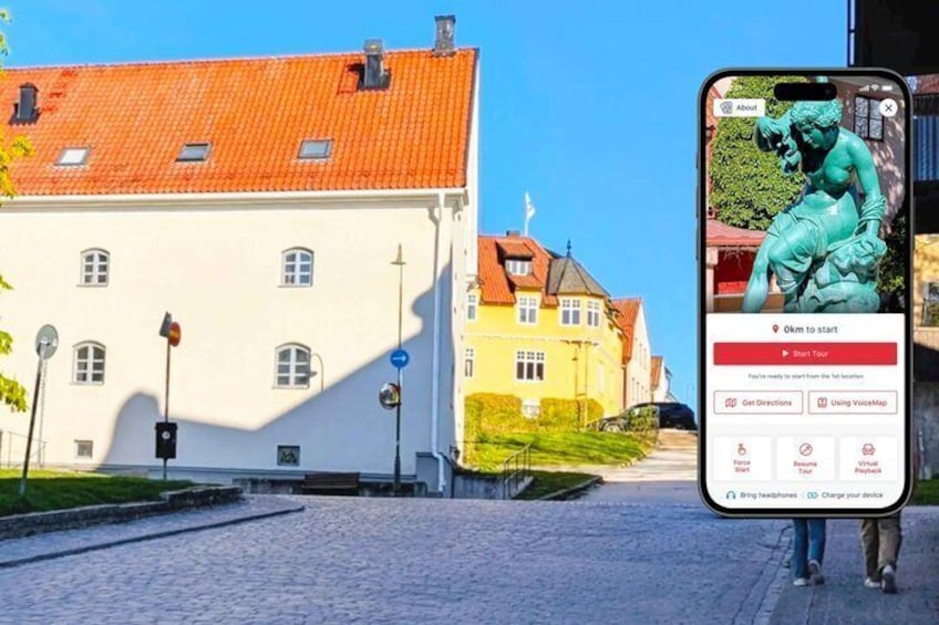 A cobblestone street with buildings, a smartphone displaying a map, and a statue. 1
