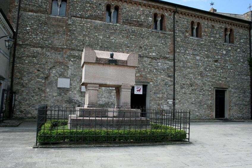 A stone building with a statue in front, surrounded by a metal fence and greenery. 3