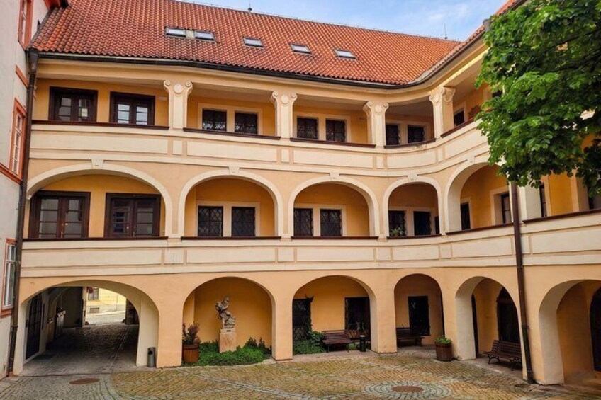 A courtyard with a yellow building, arches, a statue, and a tree. 2