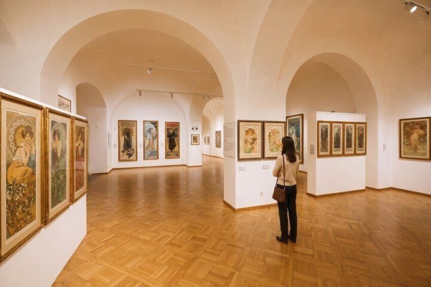 An art gallery with wooden floors and white walls, featuring framed paintings on display. 5