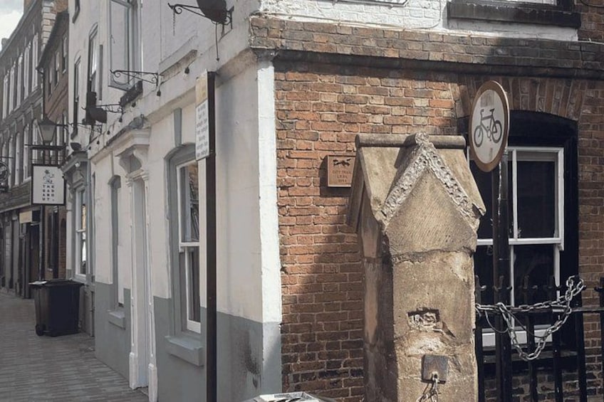 A brick building with a white door, a bicycle sign, and a small stone structure on the corner. 2