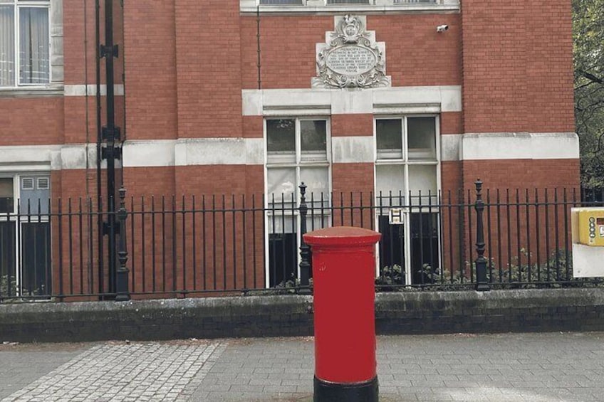 A red post box in front of a building with a brick facade and a black metal fence. 5