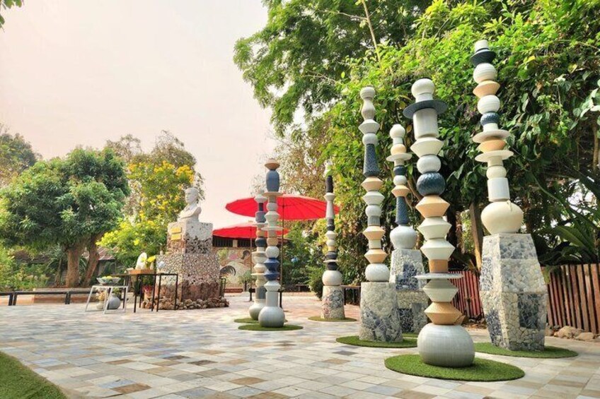 A garden with a sculpture of stacked bowls, a red umbrella, and a statue. 5