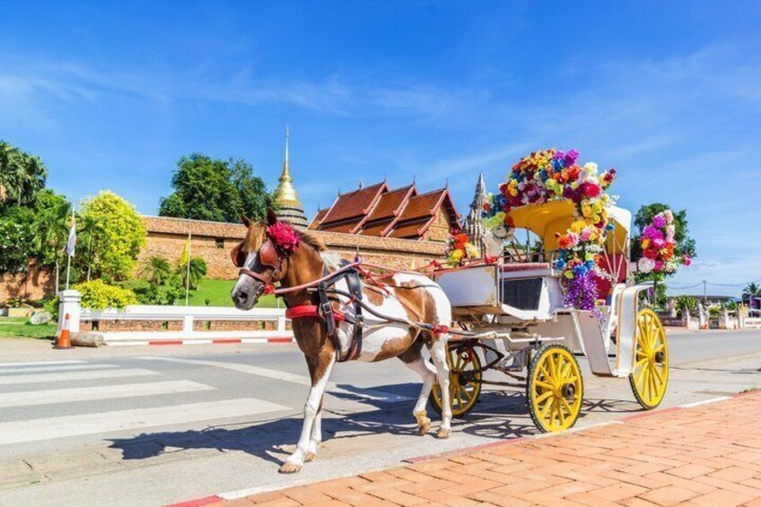 A horse-drawn carriage with yellow wheels and a floral decoration, parked on a street with a temple in the background. 1