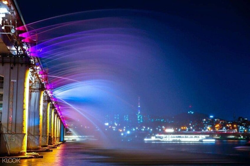 A nighttime cityscape with illuminated buildings and a waterway. 2