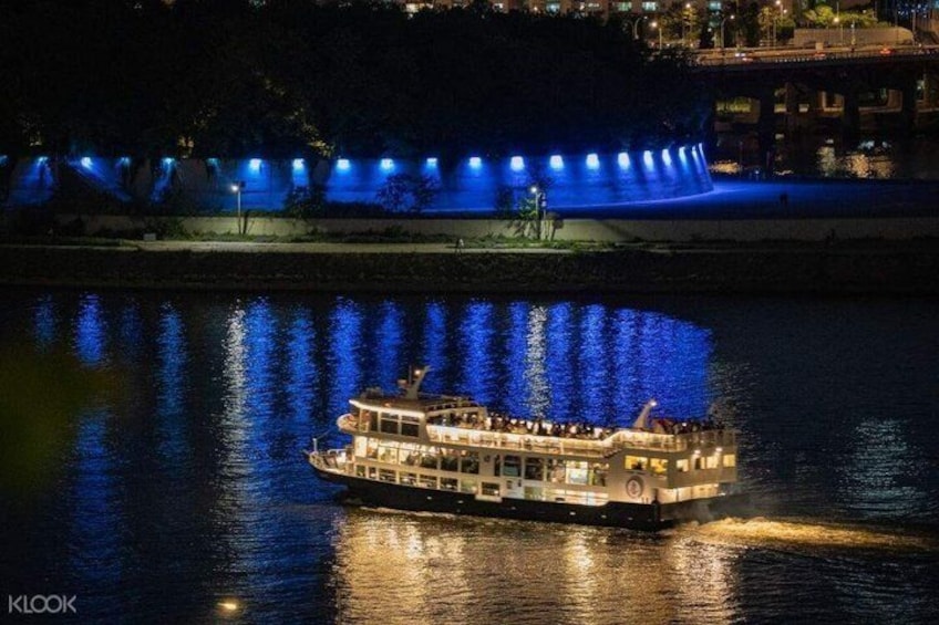 A riverboat with lights reflecting on the water, a bridge with blue lights, and buildings in the background. 4