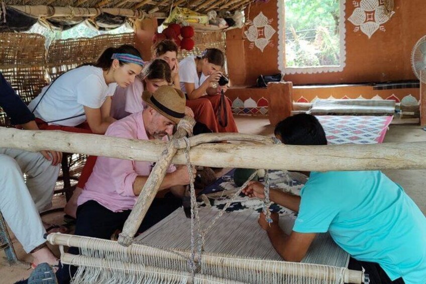 A group of people engaged in weaving on a loom, with a traditional woven mat in the foreground. 3