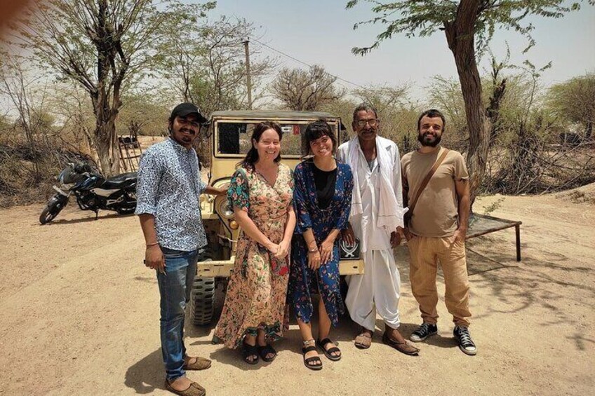 A group of people standing in a desert-like environment with sparse vegetation and a vehicle in the background. 1