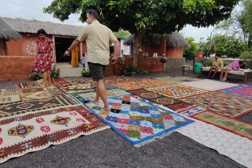 A person walking on a patterned mat, a hut, and a tree in the background. 4