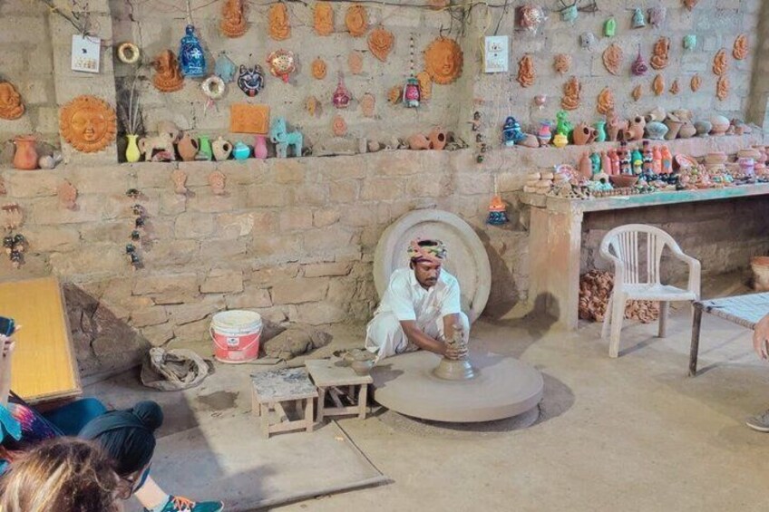 A pottery workshop with a man working on a pot, surrounded by various pottery items and tools. 2
