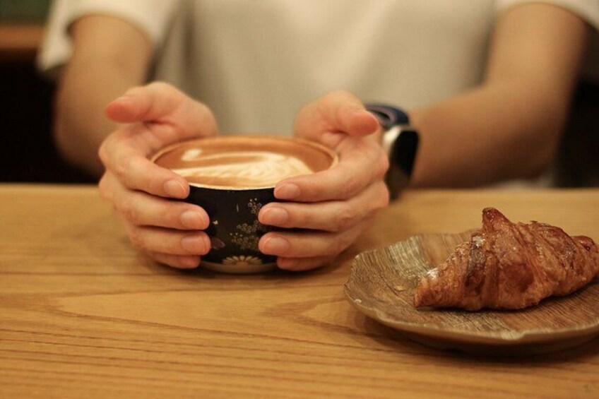 A person holding a cup of coffee and a croissant on a wooden table. 2