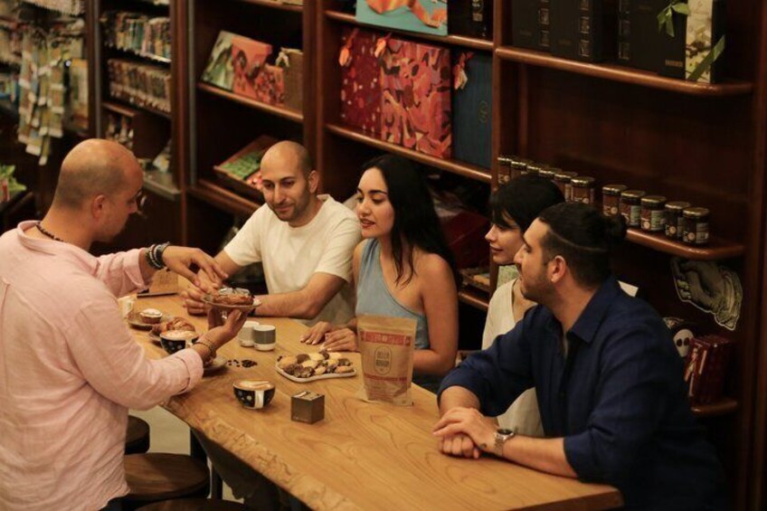 A group of people sitting around a wooden table in a bookstore, with bookshelves in the background. 1