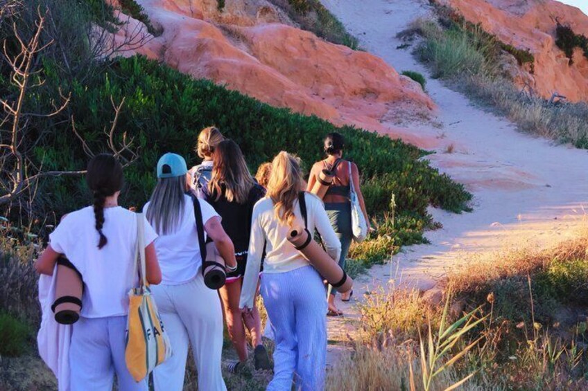 A group of people walking on a dirt path surrounded by red rock formations and greenery. 3