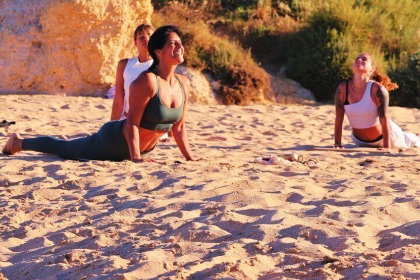 Three people doing yoga on a sandy beach with a rocky cliff in the background. 4