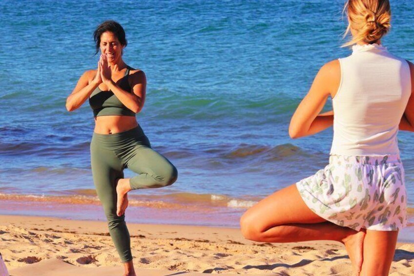 Two people practicing yoga on a beach with the ocean in the background. 1