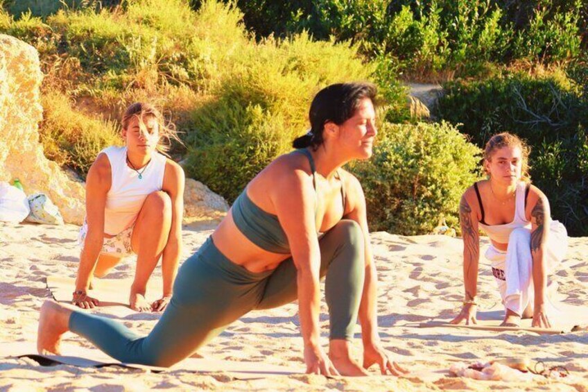 Three people performing yoga on a sandy beach with greenery in the background. 2