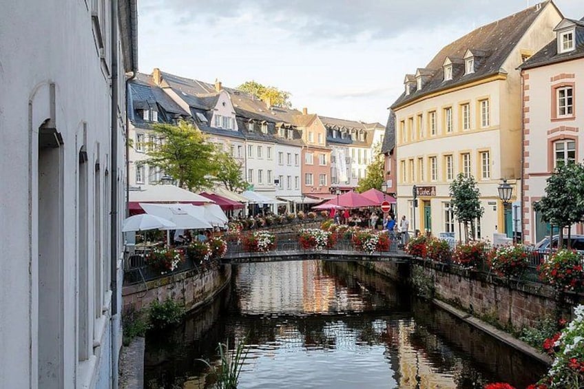 A canal with buildings on either side, a bridge, and outdoor seating with umbrellas. 1