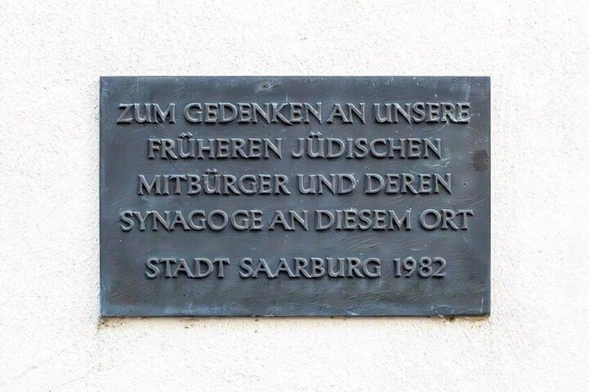 A metal plaque with text in German, mounted on a wall. 3