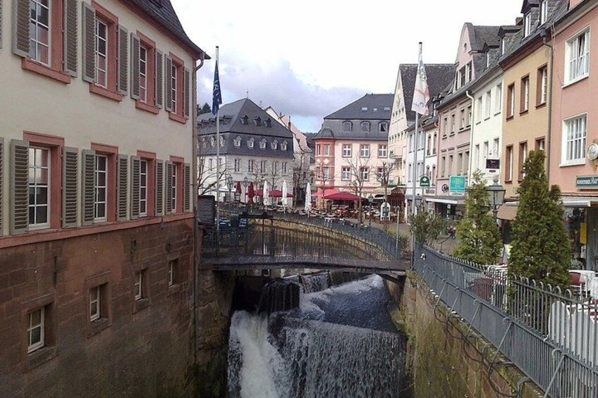 A town with a bridge over a waterfall, buildings, and a flag. 2