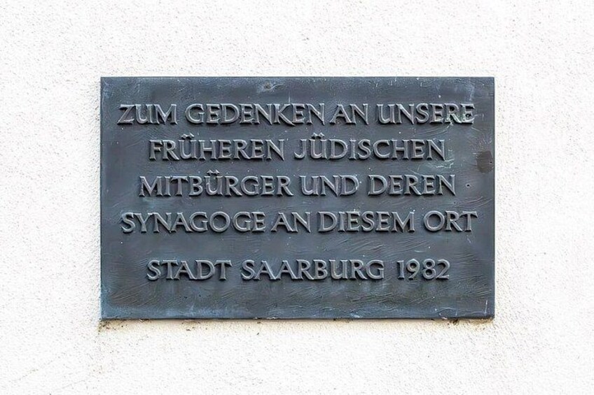 A metal plaque with text in German, mounted on a wall. 3