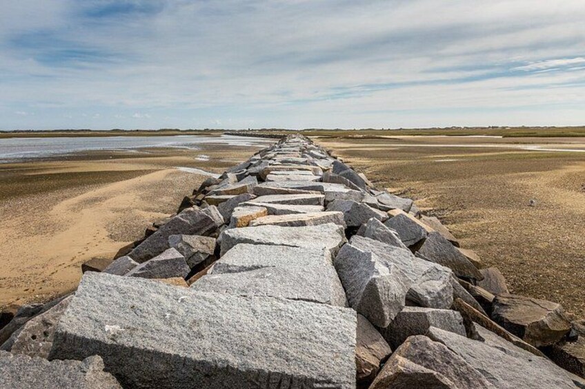 A rocky breakwater extending into a sandy beach with a calm sea in the background. 3