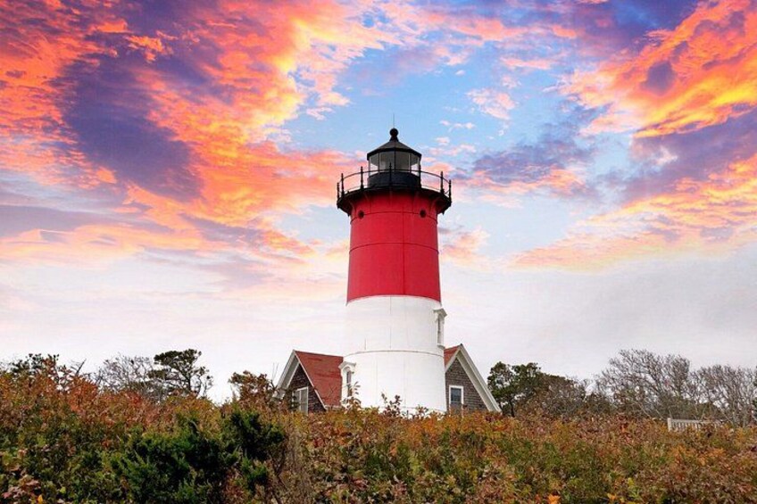 A red and white lighthouse with a white building nearby, surrounded by autumn foliage. 2