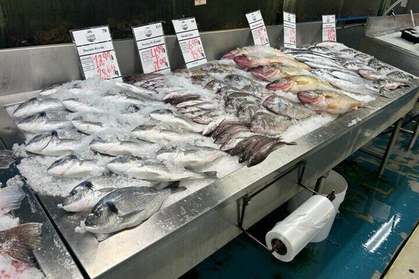 A seafood display with various fish on ice, price tags, and a blue floor. 4