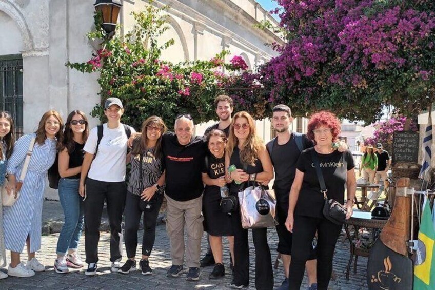 A group of people standing in a cobblestone street with historic buildings and flowering trees in the background. 1