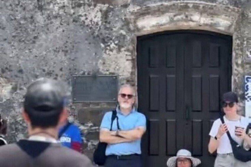 A group of people standing in front of a stone wall with a black door. 2