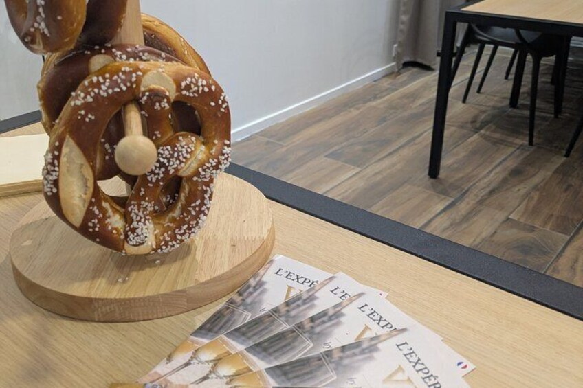 A pretzel on a wooden stand, a table with papers, and a dining area with chairs and a table. 1