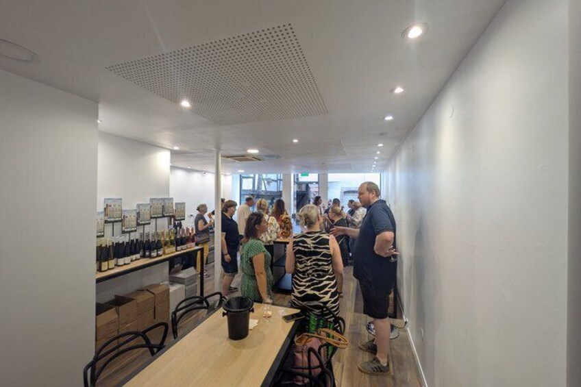 A modern interior with a long table displaying wine bottles, a ceiling with a grid pattern, and people standing and conversing. 2