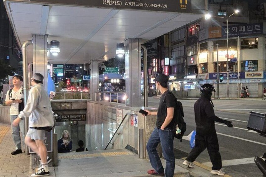 A nighttime urban scene with pedestrians, a bus stop, and illuminated storefronts. 2