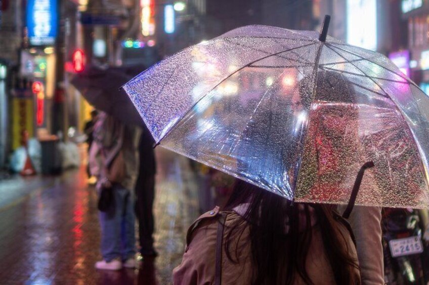 A person holding a transparent umbrella in an urban setting with wet streets and neon signs. 3