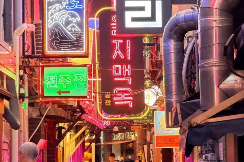 A neon-lit alley with signs in Korean, including one for a restaurant. 4