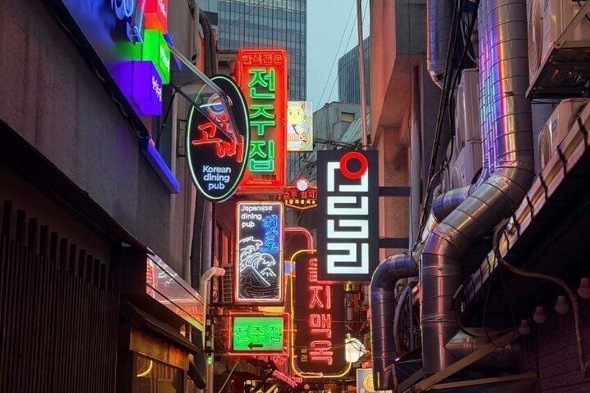 A neon-lit urban street with signs for Korean and Japanese dining pubs. 5