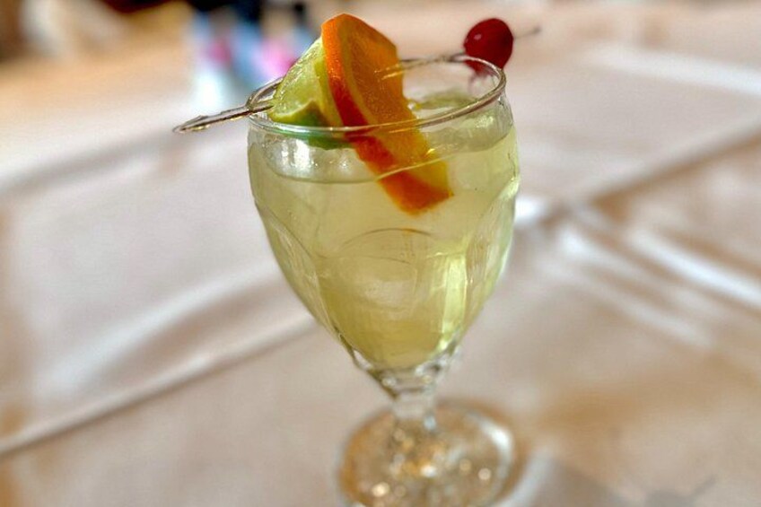 A cocktail in a stemmed glass with a slice of orange and a cherry garnish. 3