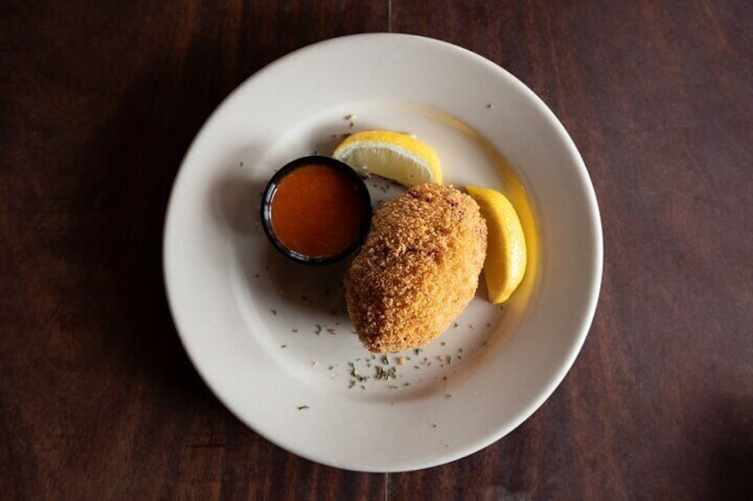 A plate with a breaded item, lemon slices, and a small bowl of sauce. 1