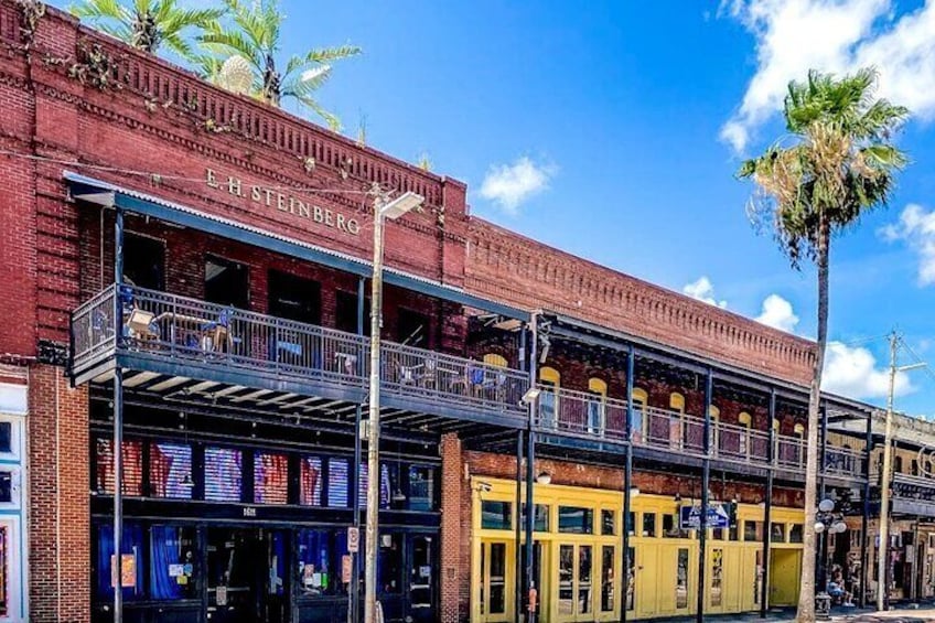 A red brick building with 'E.H. Steinberg' signage, a balcony, and a palm tree. 3