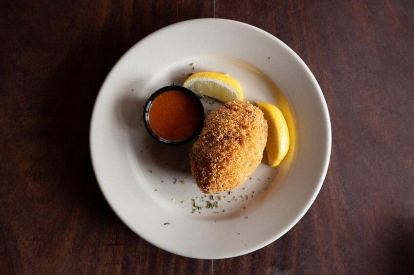 A plate with a breaded item, lemon slices, and a small bowl of sauce. 1