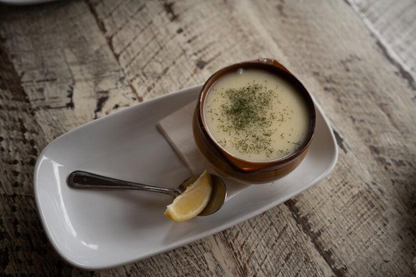 A bowl of soup on a white plate with a lemon half and a spoon. 5