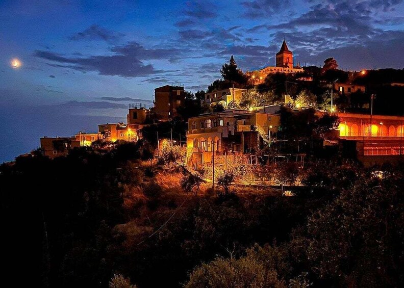 A coastal town at dusk with illuminated buildings and a prominent church on a hill. 5