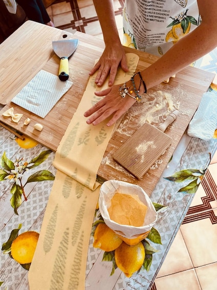 A person rolling dough on a wooden surface with a rolling pin, surrounded by lemons and a cutting board. 1