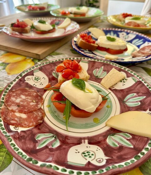 A variety of food items on decorative plates, including cured meats, cheese, and tomato-based dishes. 2