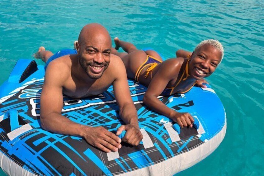Two people lying on a blue and black inflatable raft in a body of water. 1