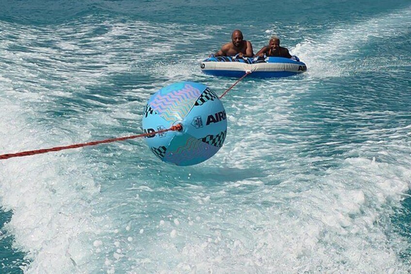 Two people on a blue inflatable raft being towed by a large blue ball with 'AIR' written on it. 5