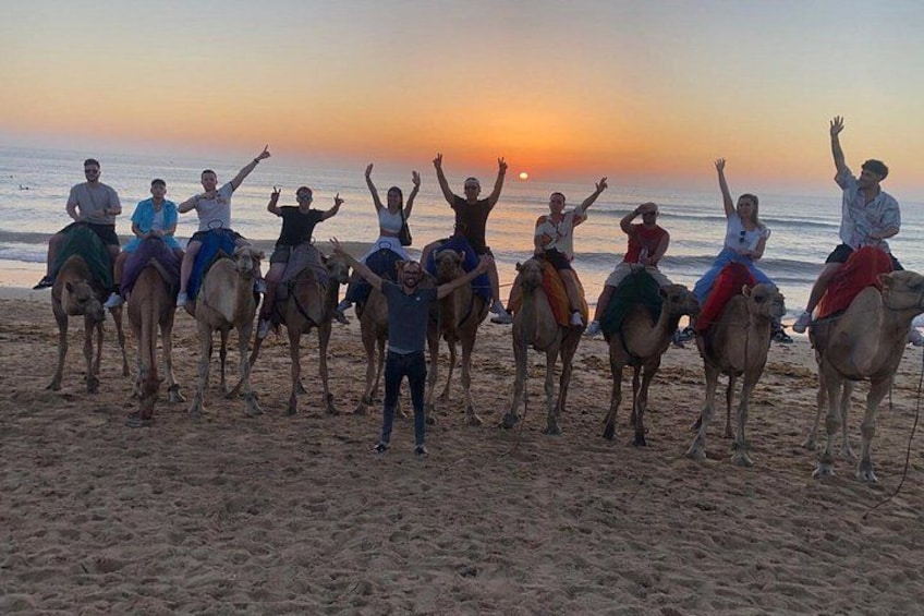 A group of people on camels on a beach at sunset. 5