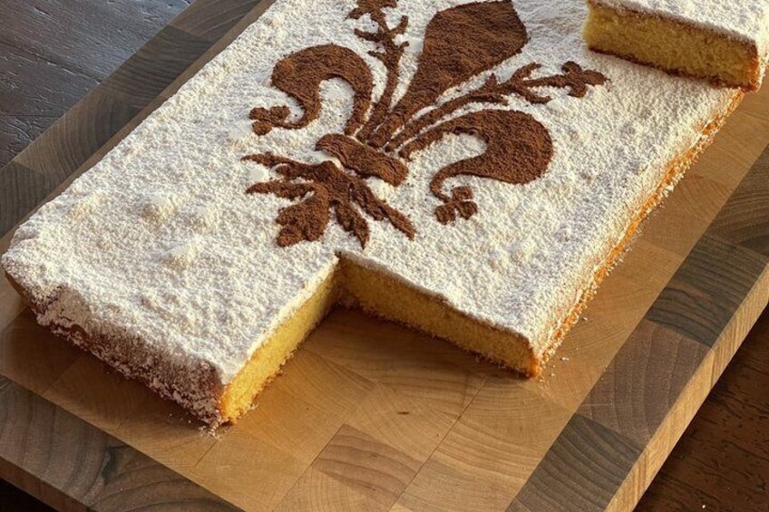 A rectangular cake with a powdered sugar design on top, placed on a wooden cutting board. 1