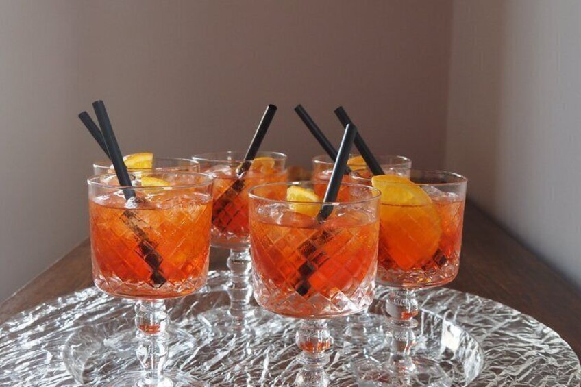 Four glasses of a red beverage with black straws and orange slices, on a textured glass table. 5