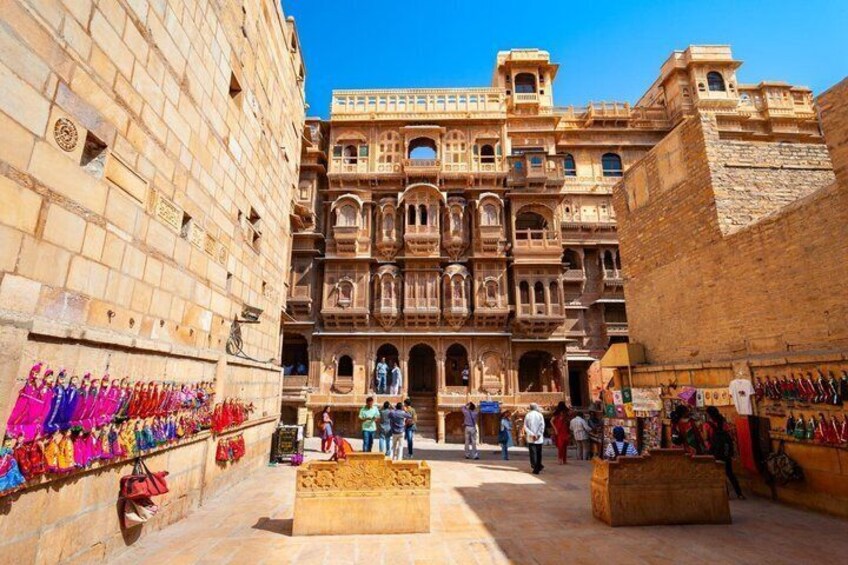 A historic building with intricate architecture, a market area with colorful textiles, and a clear blue sky. 2